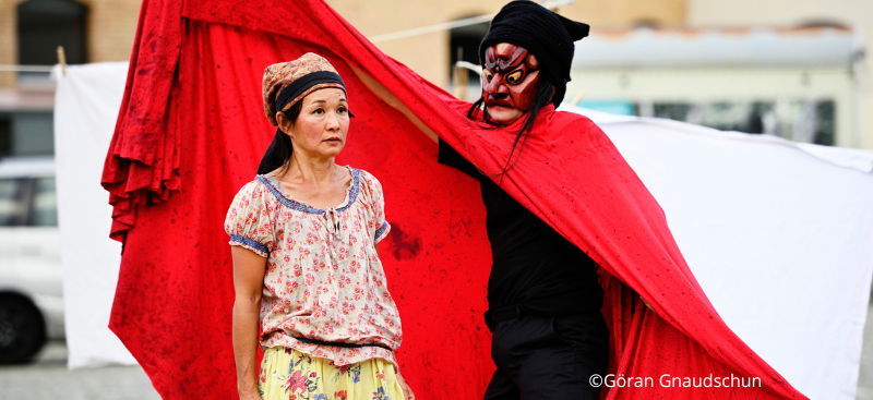 Bild: Eine Frau und ein Mann mit Maske und rotem Umhang
