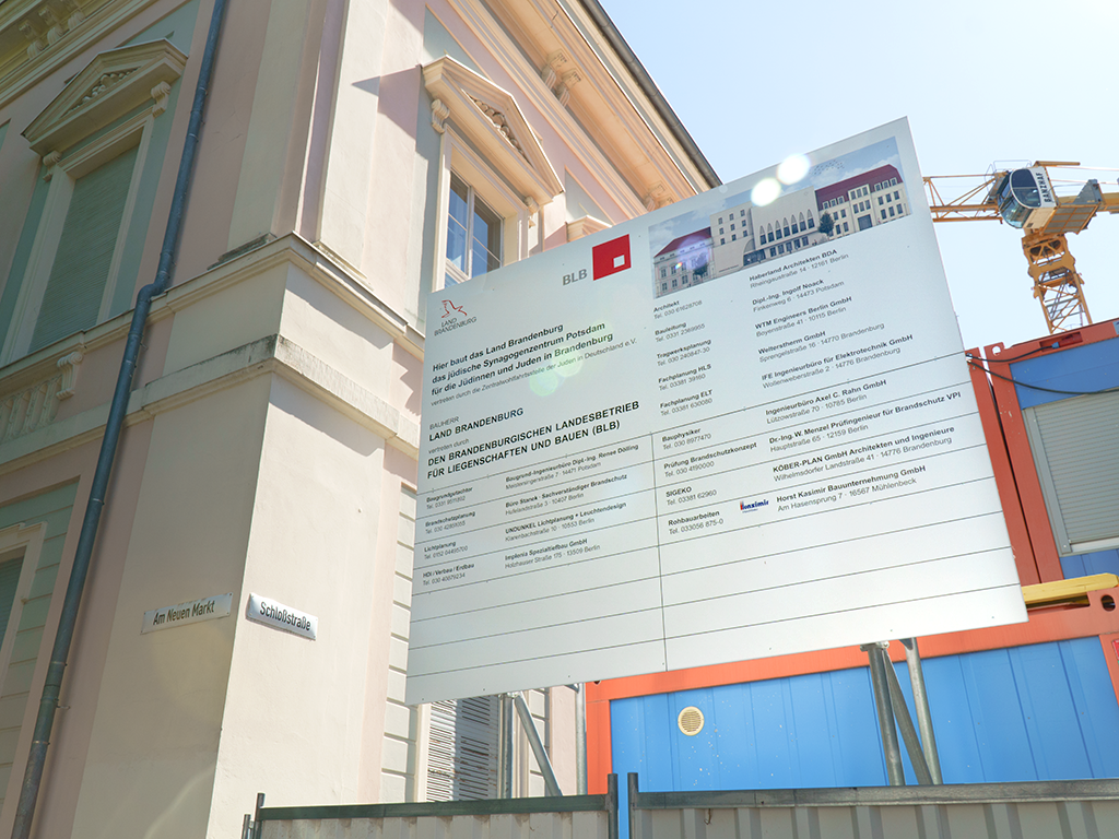 Zu sehen ist das Bauschild der neuen Synagoge in Potsdam mit Hinweisen zum Bauträger und Partnerfirmen