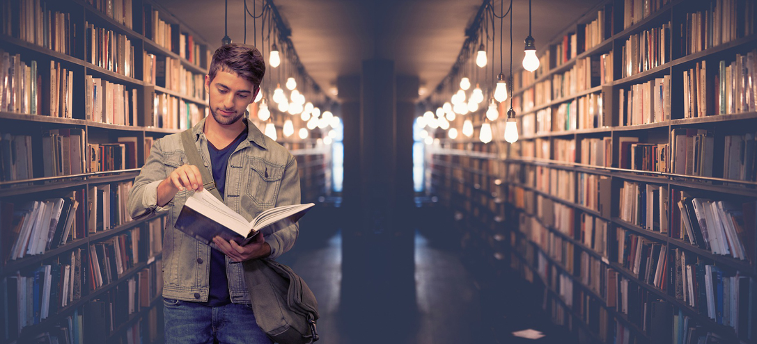 Ein männlicher Student liest in einem Buch in einer Bibliothek