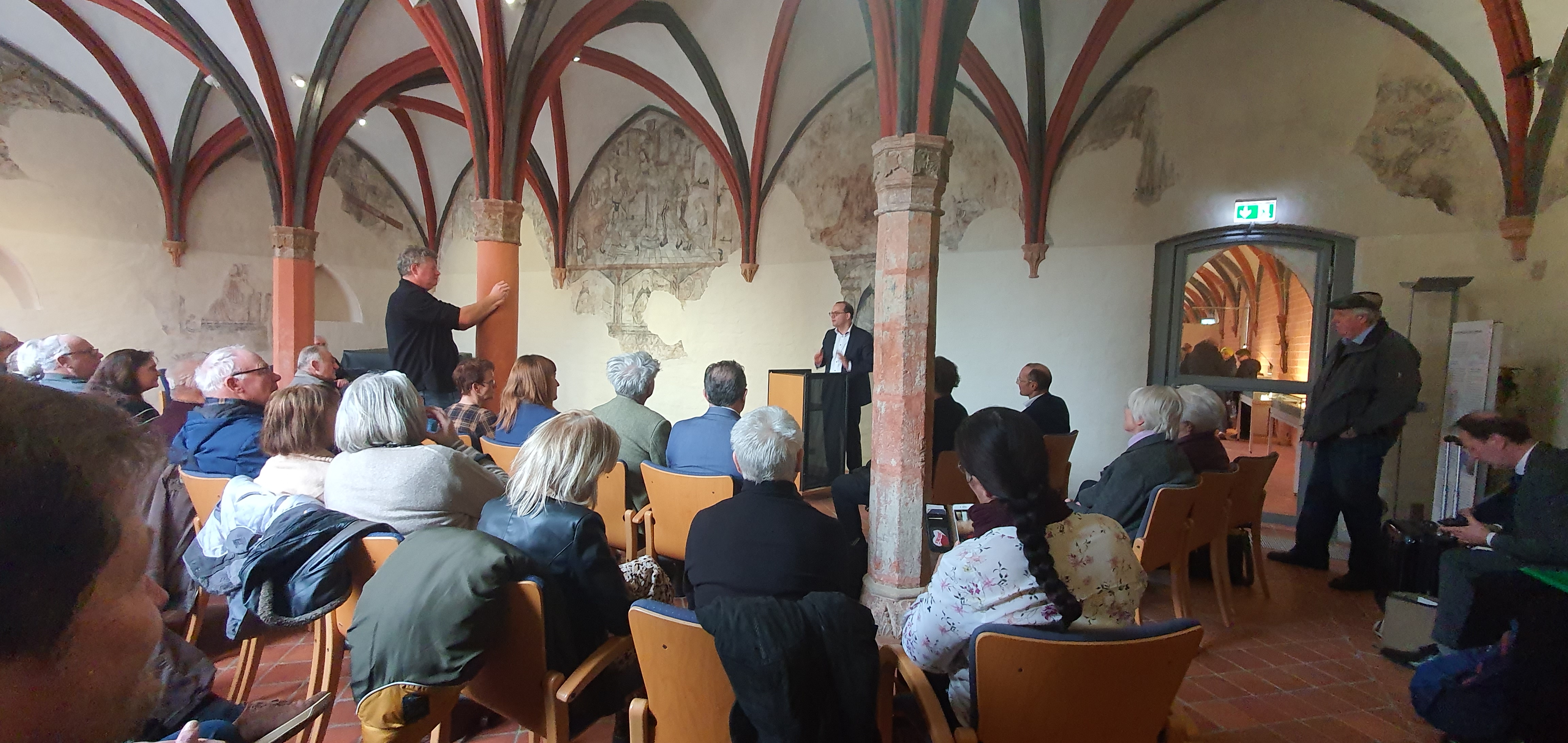 Auf dem Foto ist Staatssekretär Dünow am Rednerpult vor großem Publikum im Kloster zu sehen