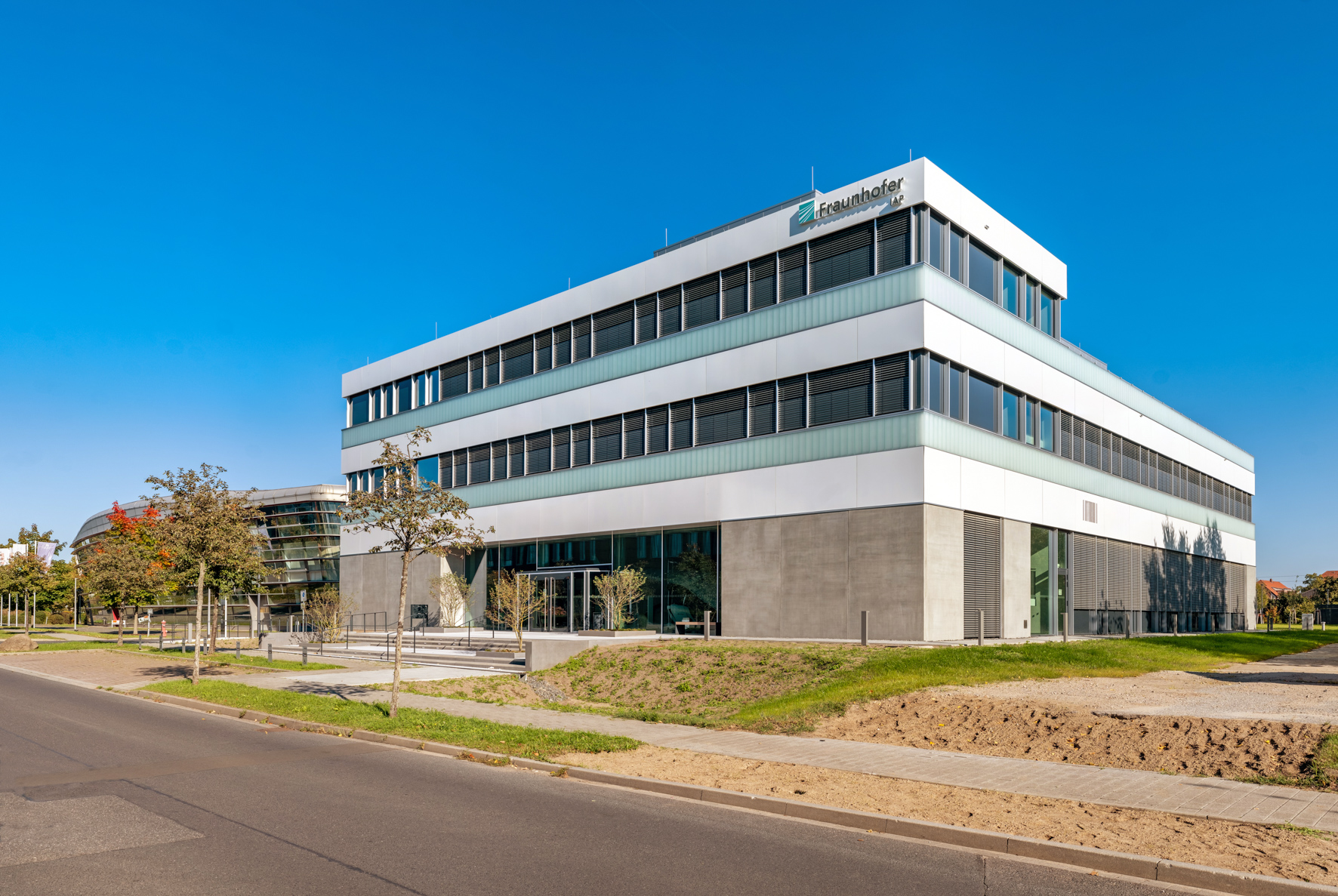 Auf dem Foto wird das neue IAP Gebäude am Standort Wildau gezeigt, weißes kastenförmiges Gebäude mit Terrassenaufsatz