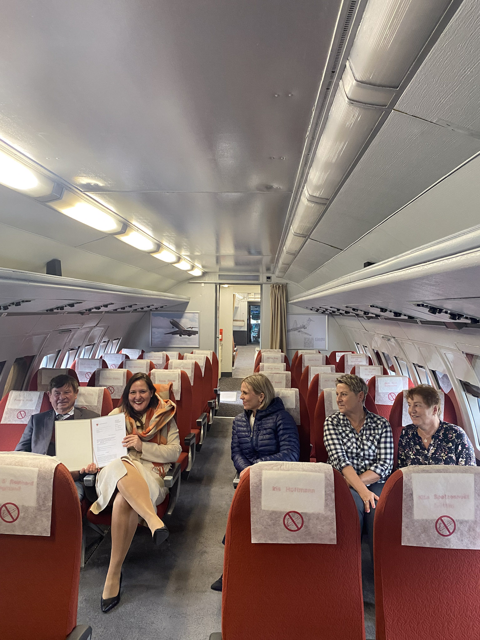 Gezeigt wird auf dem Foto Ministerin Schüle, die im Flugzeug "Lady Agnes" mit anderen Akteuren sitzt