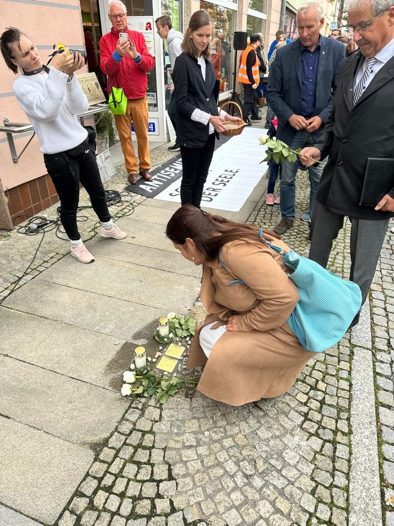 Auf dem Foto wird Ministerin Schüle gezeigt, wie sie in der Hocke Rosen auf dem Stolperstein ablegt