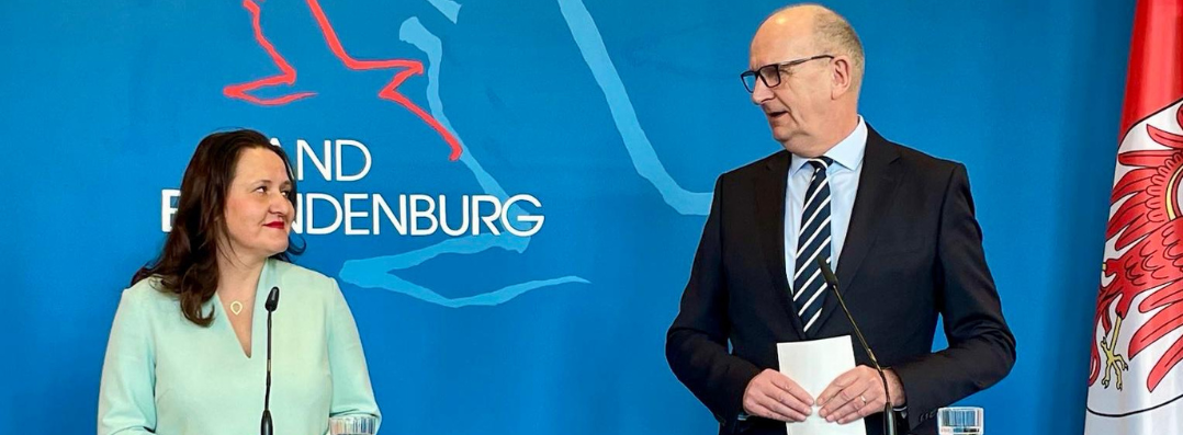 Bild: Zu sehen sind Ministerin Manja Scjüle und Ministerpräsident Dietmar Woidke vor einer blauen Wand an einem Rednerpult