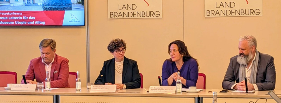 Bild: Zu sehen sind Ministerin Manja Schüle und Landrat Frank Steffen sowie Christine Gerbich an einem langen Tisch sitzend