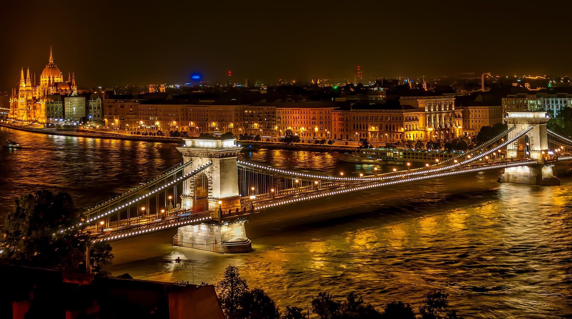 Foto zeigt die Kettenbrücke über der Donau und im Hintergrund das Parlamentsgebäude bei Nacht