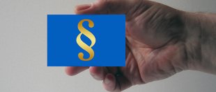 Jemand hält ein Schild mit dem Zeichen für Paragrafen abgebildet in die Kamera